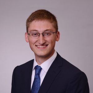 White man with crew cut and glasses wearing a suitcoat and tie.