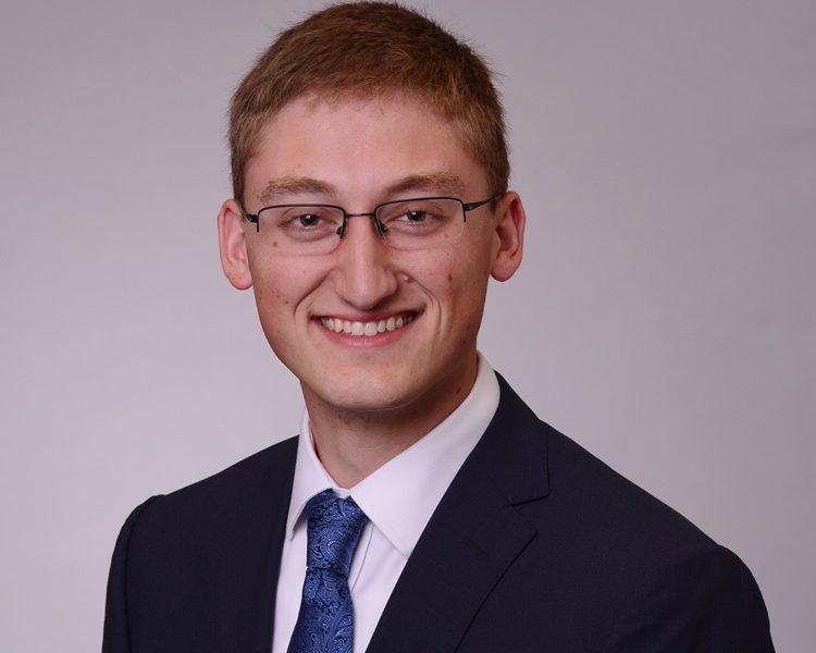 White man with crew cut and glasses wearing a suitcoat and tie.