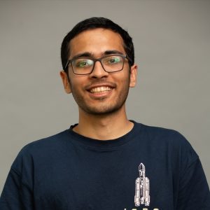 College-aged man with short dark hair and glasses wearing a dark blue t-shirt