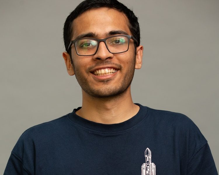 College-aged man with short dark hair and glasses wearing a dark blue t-shirt
