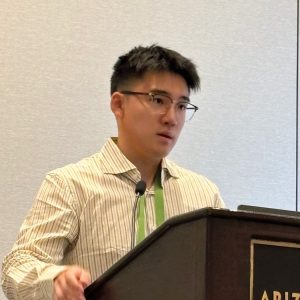 Man with dark hair and glasses making a presentation at a dais