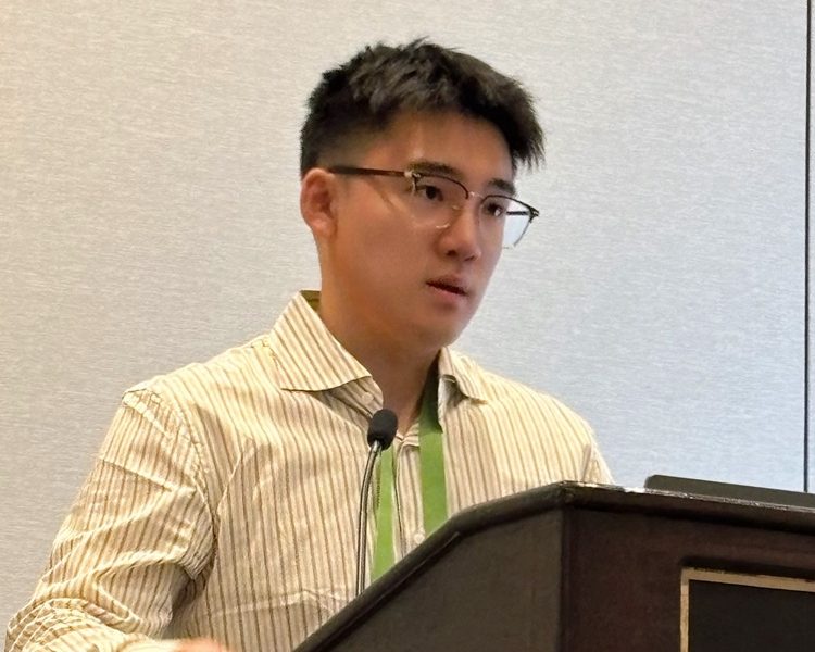 Man with dark hair and glasses making a presentation at a dais