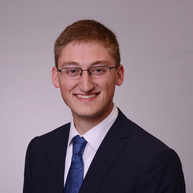 White man with crew cut and glasses wearing a suitcoat and tie.
