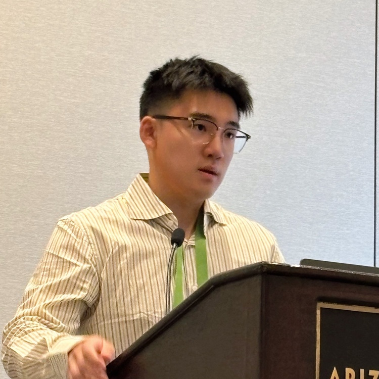 Man with dark hair and glasses making a presentation at a dais
